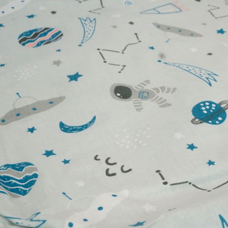 Zbliżenie bawełnianej tkaniny w jasnym kolorze z rakietami, planetami, gwiazdami i astronautą